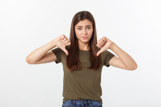 不满的女人，长长的黑发，在灰色背景上竖起大拇指向下的图片图片下载