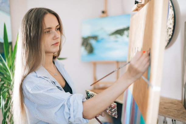 美丽的白人女性在室内绘画，使用画笔和颜料，配有平板和画架，室内氛围温馨，光线柔和图片下载