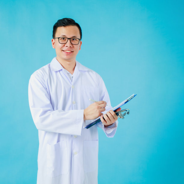 微笑的亚洲医学男性医生的肖像拿着笔记本听诊器和孤立的蓝色背景。医院有效工作理念。图片下载