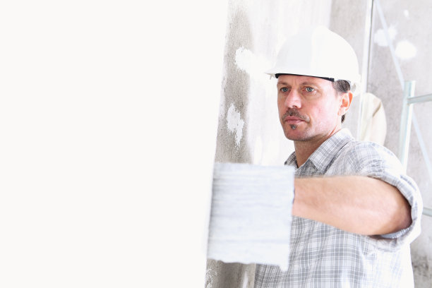 灰泥工在室内施工现场用镘刀抹灰墙面，戴安全帽和防护手套，隔离和复制空间的白墙上图片下载