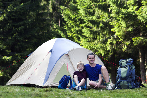 假日野营。父亲和他的儿子在森林徒步旅行和户外活动后在帐篷附近休息。幸福的家庭关系和健康的生活方式。图片下载