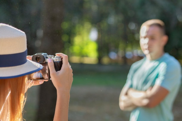 一对年轻的情侣在阳光明媚的夏日公园里拍下彼此的照片。图片下载