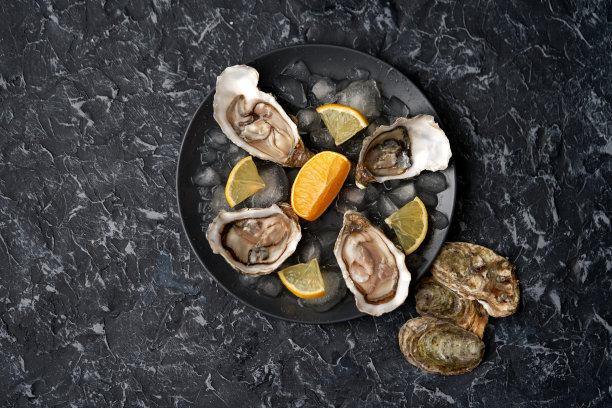 打开牡蛎与柠檬片，碎冰在一个黑色的盘子上，黑色的石头背景牡蛎壳。俯视图，处有题字，海鲜，豪华健康食品图片下载