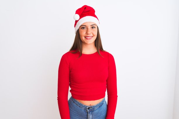 年轻美丽的女孩戴着圣诞老人的帽子站在孤立的白色背景与快乐和凉爽的微笑在脸上。幸运的人。图片下载
