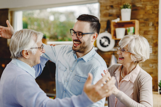 一名兴高采烈的男子在家里看望年迈的父母时问候他们。图片下载