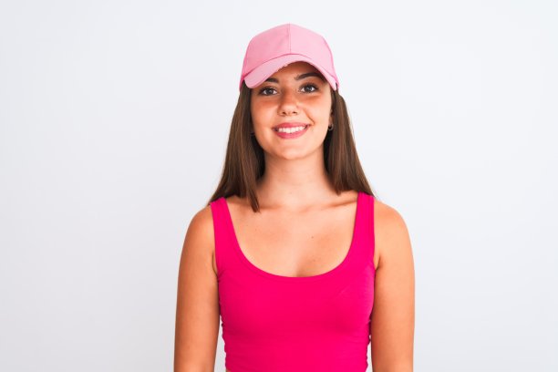 年轻美丽的女孩穿着粉红色的休闲t恤和帽子在孤立的白色背景与快乐和凉爽的微笑在脸上。幸运的人。图片下载