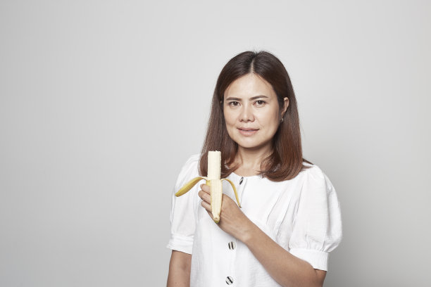 一个年轻的女人在灰色的背景下拿着香蕉黄色的生肉图片下载