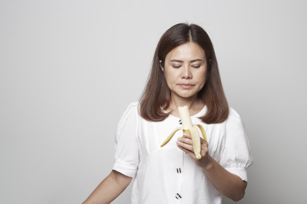 一个年轻的女人在灰色的背景下拿着香蕉黄色的生肉图片下载