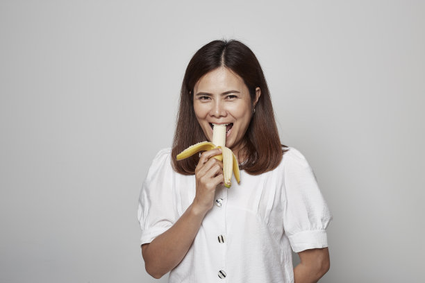 一个年轻的女人在灰色的背景下拿着香蕉黄色的生肉图片下载