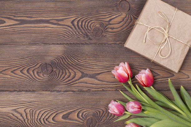 红色郁金香和牛皮纸包裹的盒子放在棕色的木桌上，放置文字图片下载