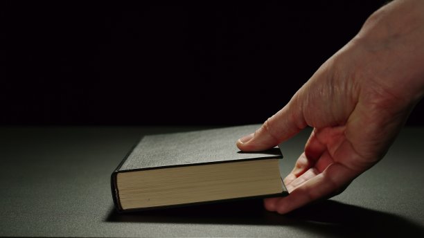 一个人把一本厚厚的黑书放在黑色的表面上图片下载