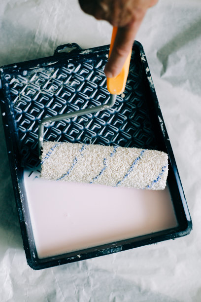 在用油漆涂墙之前，先在黑色塑料容器中的液体底漆中浸湿滚筒图片下载