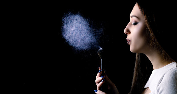 脸的侧面一个美丽的女孩吹在刷子上的化妆品，粉云与闪闪发光的黑色黑色的背景，时尚的肖像一个年轻的女人与化妆，女性的美丽概念图片下载