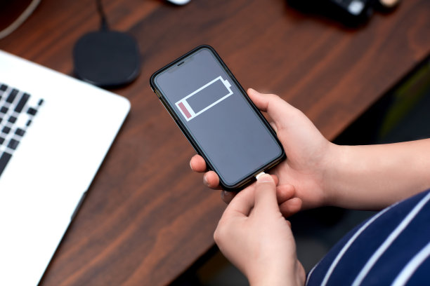 The man's hand connects the charger to his smartphone, with an office desk in the background。图片下载