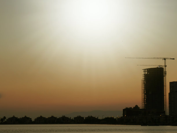 建筑与摩天大楼和起重机映衬着阳光下五彩缤纷的天空。图片下载