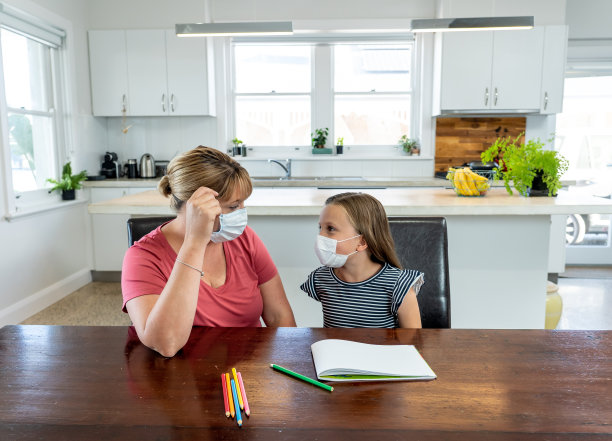 新冠疫情爆发：封锁和停课，母亲帮助戴口罩的女儿在家上网课图片下载
