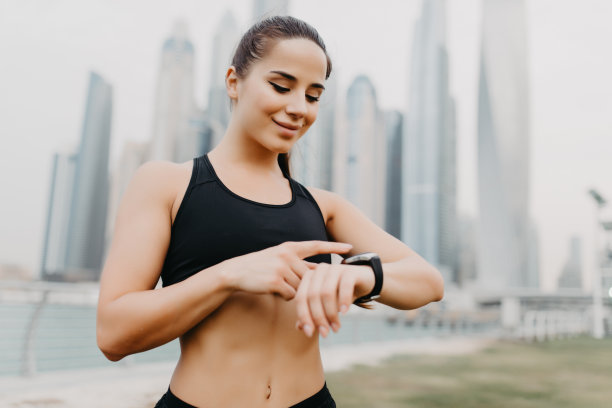 年轻女人设置健身智能手表，准备在摩天大楼背景下跑步。女运动员检查手表设备图片下载