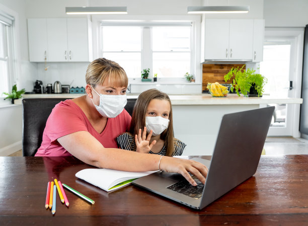 新冠疫情爆发：封锁和停课，母亲帮助戴口罩的女儿在家上网课图片下载