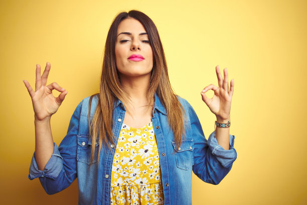 年轻美丽的女人站在黄色孤立的背景放松和微笑，闭上眼睛做冥想手势与手指。瑜伽的概念。图片下载