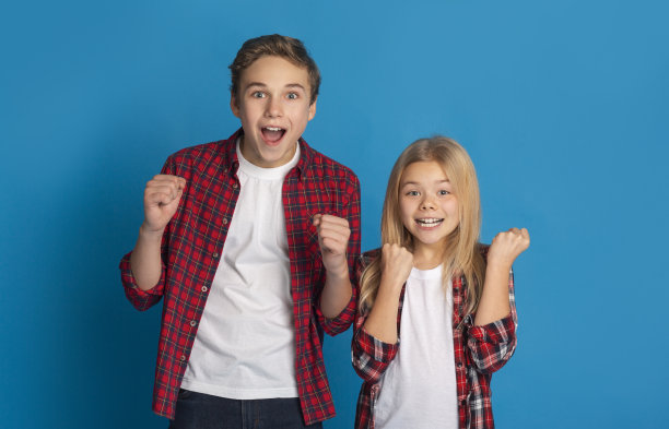 兴奋的男孩和女孩庆祝成功，在蓝色背景上举起拳头图片下载