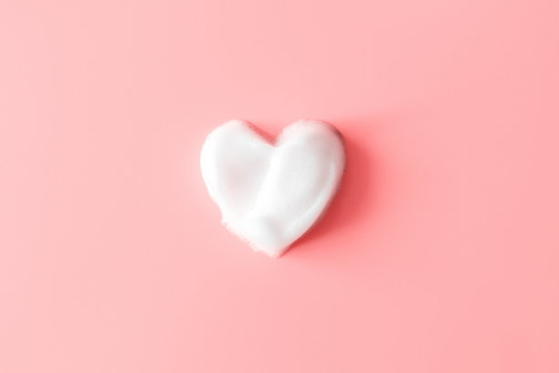 粉色背景上的肥皂泡沫上的心。白色的清洁剂纹理。概念卫生和保健图片下载