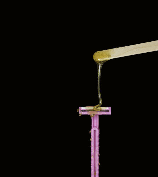 糖糊或美容蜡从木质上蜡板流到粉色剃须机。脱毛的概念。蜡和剃须刀。黑色背景。图片下载