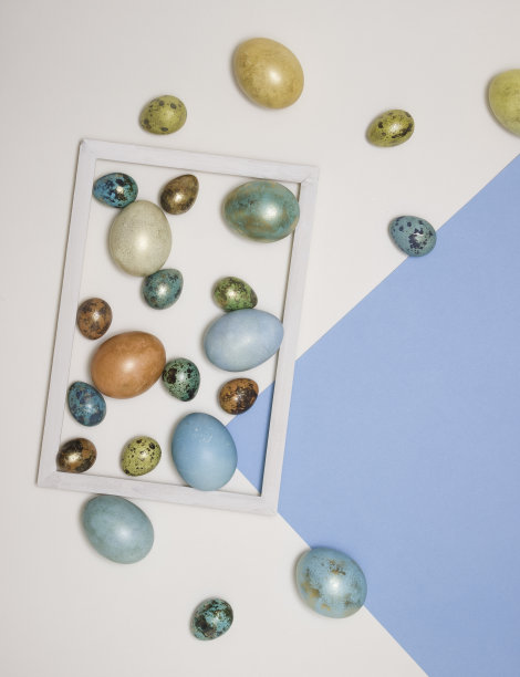 彩色的复活节彩蛋在一个木制的白色框架，并在它旁边的白色和蓝色的背景。文本的空闲空间。图片下载