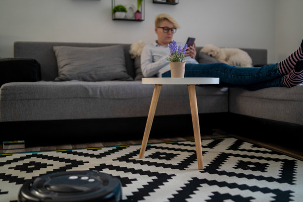 女人在沙发上休息时，机器人吸尘器正在清洁房间特写图片下载