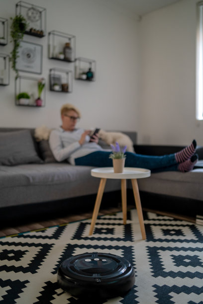 女人在沙发上休息时，机器人吸尘器正在清洁房间特写图片下载