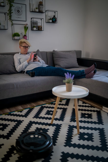 女人在沙发上休息时，机器人吸尘器正在清洁房间特写图片下载