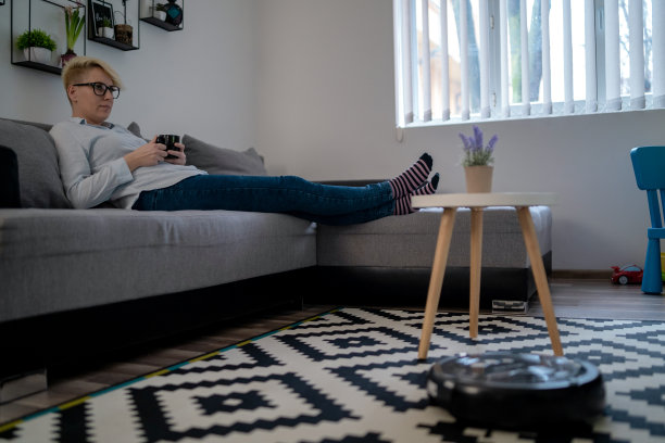 女人在沙发上休息时，机器人吸尘器正在清洁房间特写图片下载