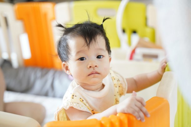 可爱的8个月大女婴站立在家中儿童隔断背景前观看某物竖版照片图片下载