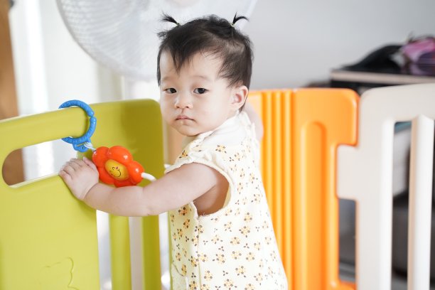 可爱的8个月大女婴站立在家中儿童隔断背景前观看某物竖版照片图片下载