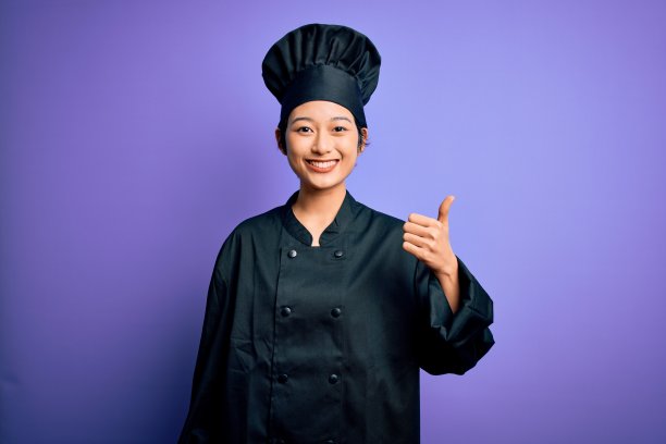 一位年轻漂亮的中国女厨师穿着厨师制服和帽子，在紫色背景前竖起大拇指，面带微笑，看着镜头，表达赞许和成功。图片下载