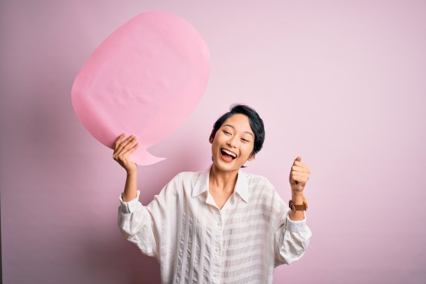 年轻漂亮的亚洲女孩拿着语音泡泡在粉红色背景上尖叫，自豪地庆祝胜利和成功，非常兴奋，欢呼雀跃素材图片