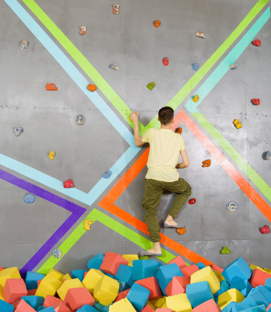 青少年男孩在蹦床中心攀岩墙上。青少年的冒险和极限概念图片下载