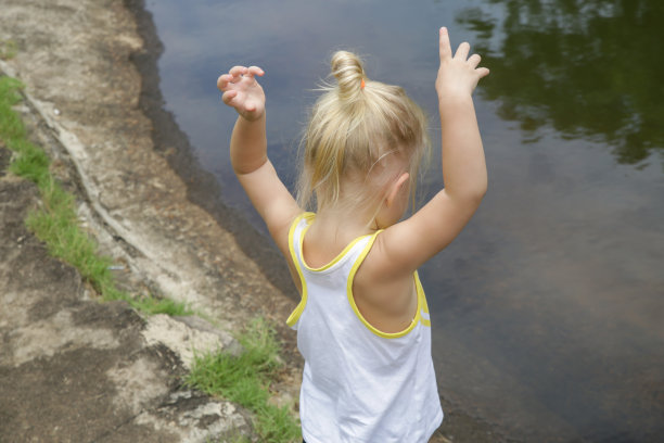 快乐的小女孩双手举在一个大水坑前，两岁的小女孩在户外打发时间图片下载