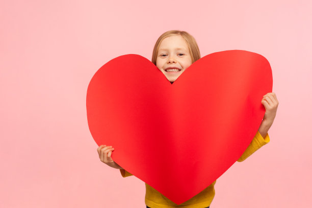 甜美可爱的小女孩的肖像从大红心标志和微笑的相机图片下载