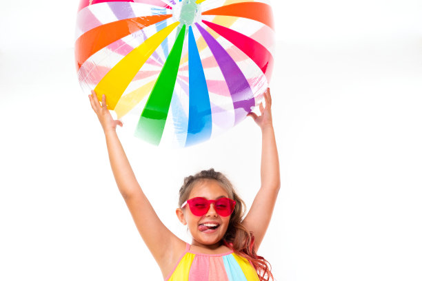 十几岁的白人女孩与色彩鲜艳的衣服持有大橡胶球孤立的白色背景图片下载