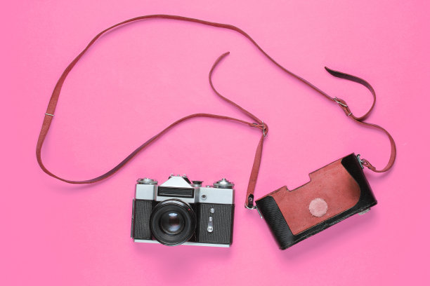 旅游极简主义的概念。复古复古的胶片相机和皮革封面与皮带在粉红色的背景。俯视图图片下载