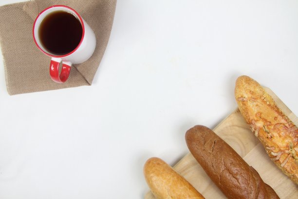 三根长棍面包放在木砧板上，一杯茶放在白色背景的帆布餐巾上。水平的形象图片下载