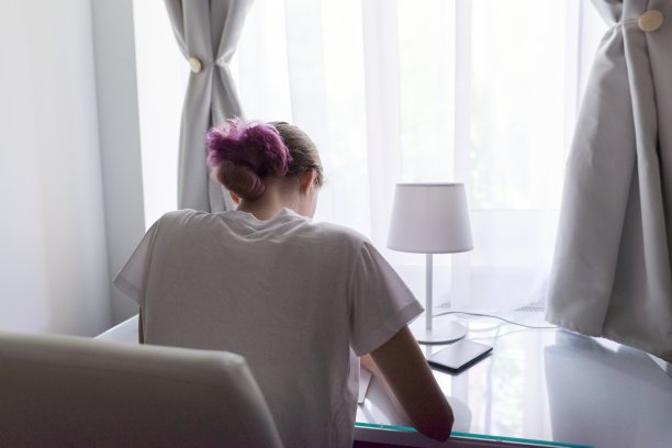 女孩坐在靠近窗户的书桌旁，后视图，学生在家里学习图片下载