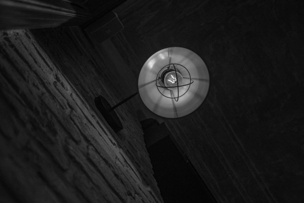 黑白照片的圆形金属灯罩与玻璃灯泡内。复古金属灯的特写，暗模糊的背景，旧的纹理砖墙。室内照明复古装饰。图片下载