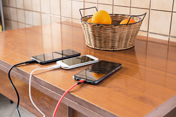厨房桌子上的三部智能手机正在充电，屏幕上有反光图片下载