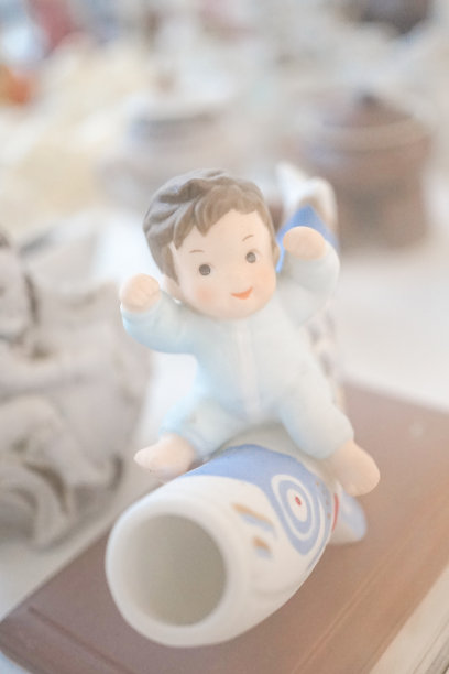 小男孩身穿浅蓝色婴儿装骑在锦鲤或鲤鱼上的微雕，柔软的对焦滤镜营造出柔和梦幻的效果。图片下载