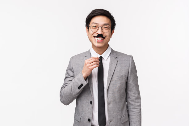 穿着灰色西装，拿着带胡子的棍子，在办公室聚会上微笑的滑稽英俊亚洲男子半身像，与同事庆祝节日，白色背景图片下载