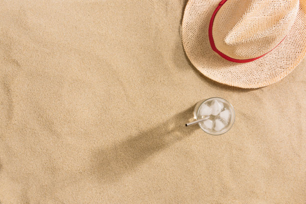 暑假的作文。帽子和一杯有冰的水，背景是沙子。强光和阴影。夏天的背景。图片下载