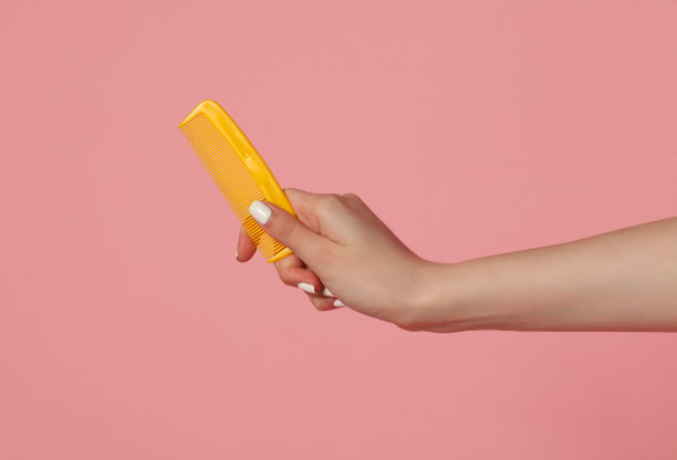 女人手持梳子，粉色背景图片下载