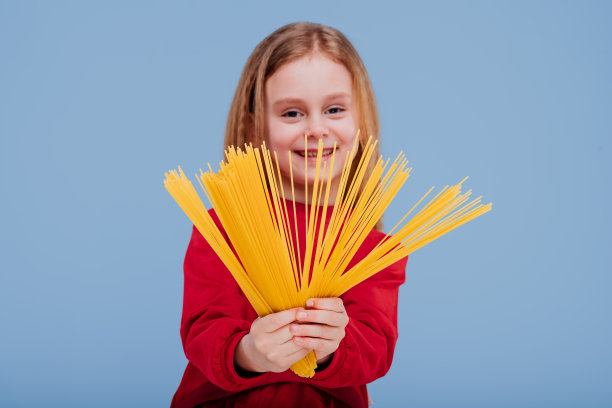 一个小女孩拿着意大利面。烹饪概念。孤立的蓝色背景近景图片下载
