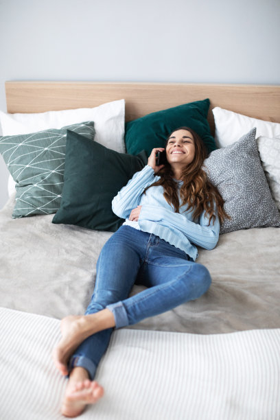 年轻漂亮的女人躺在沙发上打电话。图片下载